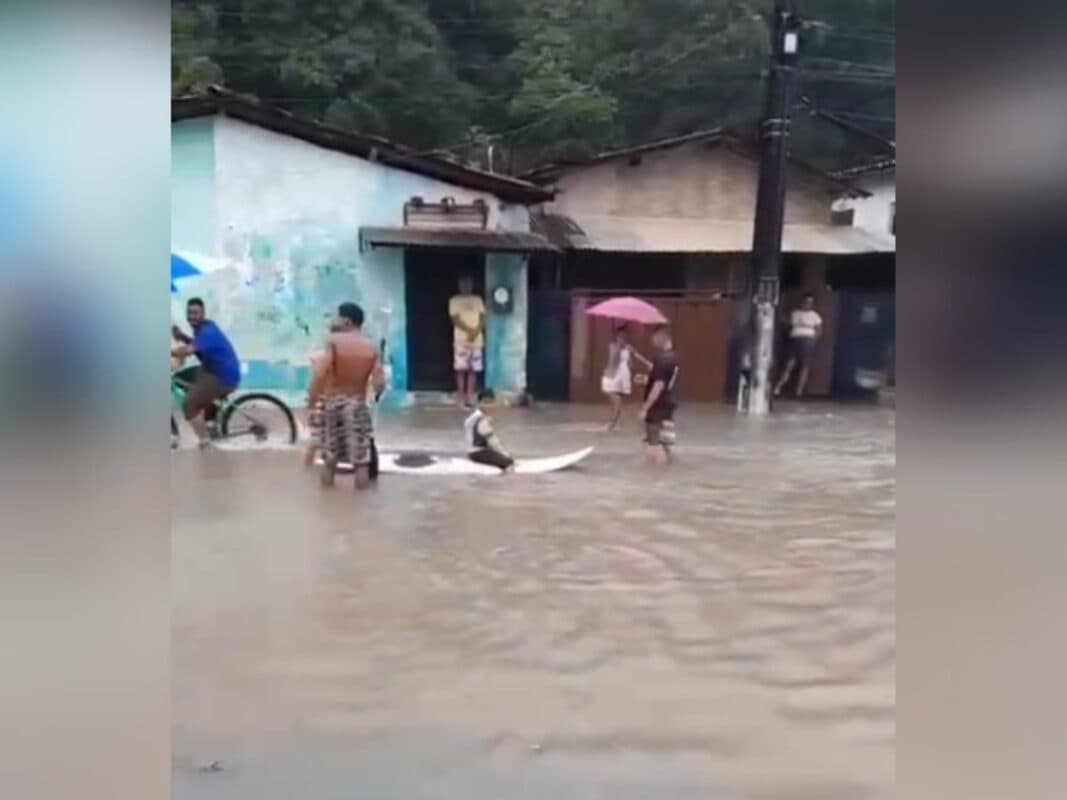 Crianças brincam em prancha de surfe durante alagamento no Bairro São José, em João Pessoa